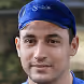 Portrait d’un homme portant un bandana bleu, souriant légèrement avec un fond flou.